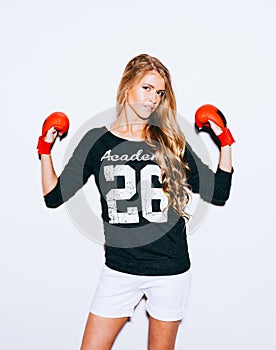 Beautiful blond girl in red boxing gloves posing on a white background. Lifted hands. Indoor. Warm color.