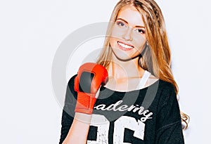 Beautiful blond girl in red boxing gloves posing on a white background. She raised one arm. Close up. Indoor. Warm color.