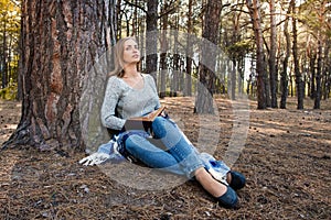 Beautiful blond girl resting in spring or autumn forest read book and sitting with a book. Confident caucasian young