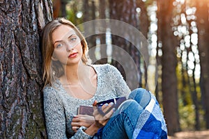 Beautiful blond girl resting in spring or autumn forest read book and sitting with cup of tea and book. Confident