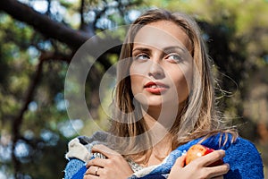 Beautiful blond girl resting in spring or autumn forest with red apple in her hands. Confident caucasian young woman in