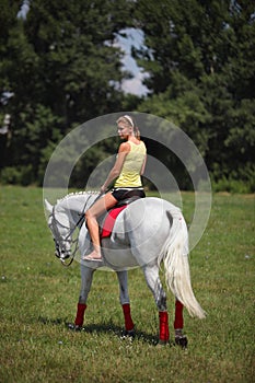 Beautiful blond girl riding horseback in summer meadow