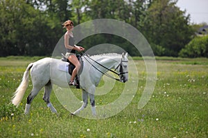 Beautiful blond girl riding horseback in summer meadow