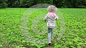 Beautiful blond girl run through meadow in park. Lovely child have fun outdoors