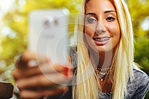 Amused blond girl with braces using cell phone photo