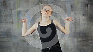 Beautiful blond hair teen girl dancing hiphop on the gray wall. Actively works with hands.