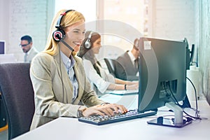 Beautiful blond haired business woman working in customer support center at the workplace with colleagues in the office