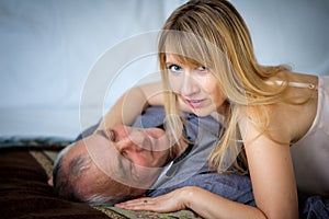 Beautiful Blond-Haired Woman in Lingerie Hugging Her Senior Husband Lying in Bed. Couple with Age Difference.