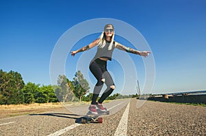 Beautiful, blond hipster with blue hair in a tattoo is riding a longboard.