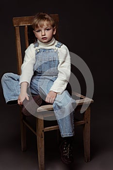 Beautiful blond little girl sitting on the old chair with sad expression on her face