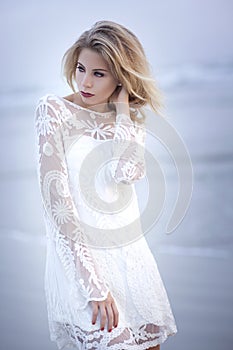 Beautiful blond model on the beach with flowing hair in wind and white lace dress.