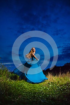 Beautiful blond model in blue air dress posing on the green meadow