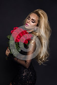 beautiful blond model in elegant dress holding a bouquet of red roses. Valentines`s gift on a black background