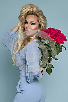 Beautiful blond model in elegant dress holding a bouquet of roses . Valentine`s and birthday gift on a blue background