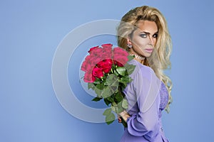 Beautiful blond model in elegant dress holding a bouquet of roses . Valentine`s and birthday gift on a blue background
