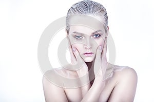 Beautiful blond model with nude make up, slicked back hair and naked shoulders holding her face in her hands