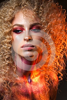 Beautiful blond model with a very volume curl hairstyle, colorful red smoky eyes and body art