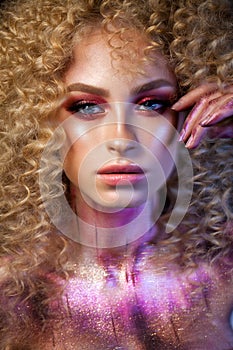Beautiful blond model with a very volume curl hairstyle, colorful red smoky eyes and elements of body art