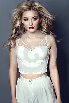 Beautiful blond model wearing white summer high waisted pants and corset strapped top