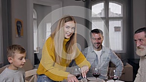 Beautiful blond mother in knitted yellow sweater looking at camera while slicing roast turkey for her family during