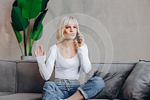 Beautiful blond pensive girl sitting on the sofa and talking on the phone