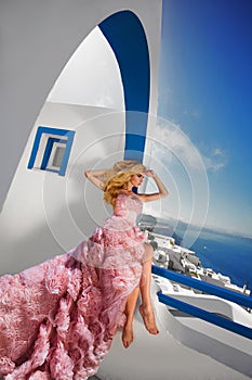 Beautiful blond runaway bride in white wedding dress fabulous with a very long train of crystals in the street on Santorini