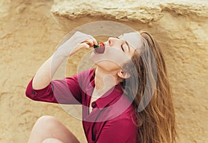 Beautiful blond smiling girl in purple dress eating fresh strawberry