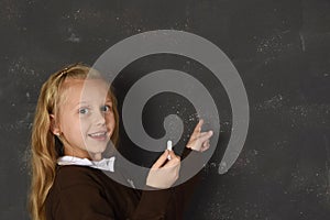 Beautiful blond sweet schoolgirl in uniform holding chalk writing on blackboard smiling happy