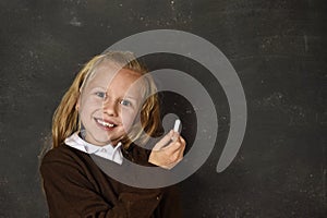 Beautiful blond sweet schoolgirl in uniform holding chalk writing on blackboard smiling happy