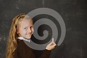 Beautiful blond sweet schoolgirl in uniform holding chalk writing on blackboard smiling happy