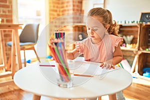 Beautiful blond toddler girl drawing with colored pencils at kindergarten
