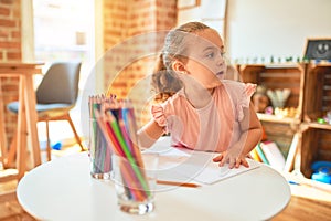 Beautiful blond toddler girl drawing with colored pencils at kindergarten