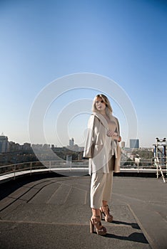 Beautiful blond woman in beige coat standing on the roof top of the house.