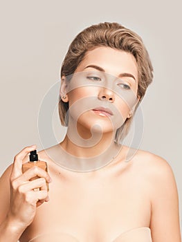 beautiful blond woman with bottle of perfume on beige background. Model with nude makeup, retouched studio shot