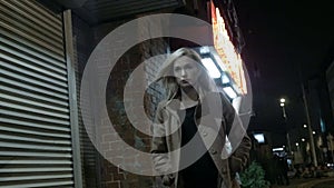 Beautiful blond woman in coat walking alone outdoors at night. Grain. Slow motion.