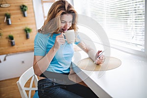 Beautiful blond woman drinking coffee and reading news