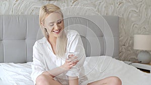 Beautiful blond woman drinking a coffee while sitting on her bed at home