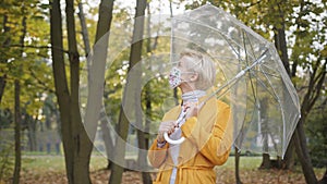 Beautiful blond woman with face mask spinning transparent umbrela in the park in autumn. Coronavirus outbreak 2020