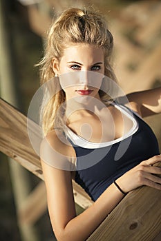 A beautiful blond woman with her hair in a pony tail sitting under pier near ocean.