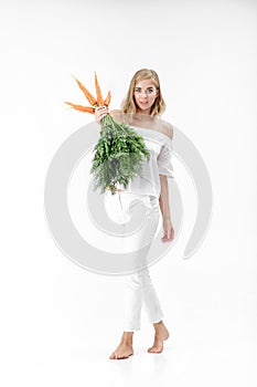 Beautiful blond woman holding fresh carrot with green leaves on white background. Health and Diet