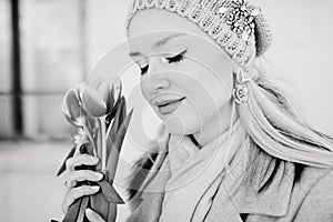 Beautiful blond woman in a knitted hat with tulip flowers. Black and white photo