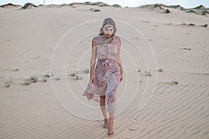 Beautiful blond woman in long dress and jewelry on her head walking in desert