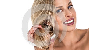 Beautiful blond woman with long hair touching her hair on whie background. Perfect smile. Copy space