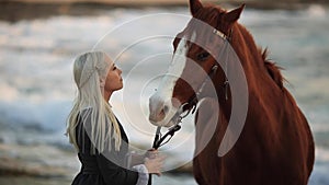 Beautiful blond woman in an old-fashioned dress embracing a brown horse