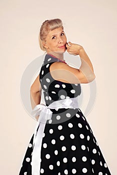 Beautiful blond woman in pinup style dressed in a polka-dot dress turns around and smiles, white background
