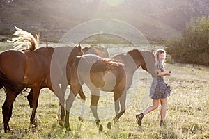 A beautiful blond woman playing with horses in a field.