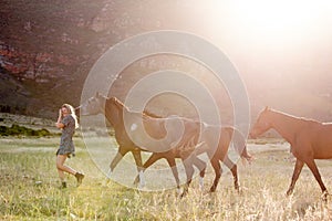 A beautiful blond woman playing with horses in a field.