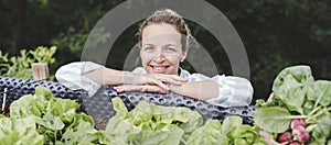 Beautiful blond woman posing next to raised garden bed and her fresh vegetables