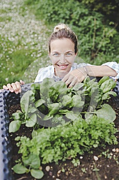 Beautiful blond woman posing next to raised garden bed and her fresh vegetables