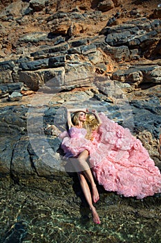 Beautiful blond woman pink ballroom dress standing on the rocks in Santorini